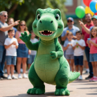 A friendly green baby T-Rex mascot waving to visitors